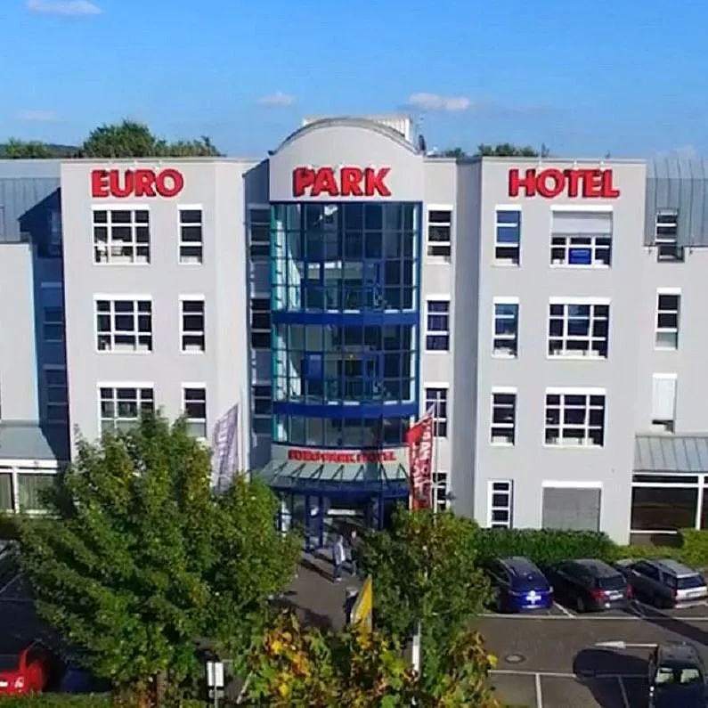 Luftbild des EURO PARK HOTEL Hennef mit dem Haupteingang unter dem Glasturm und dem Parkplatz vor dem Haus an einem sonnigen Tag