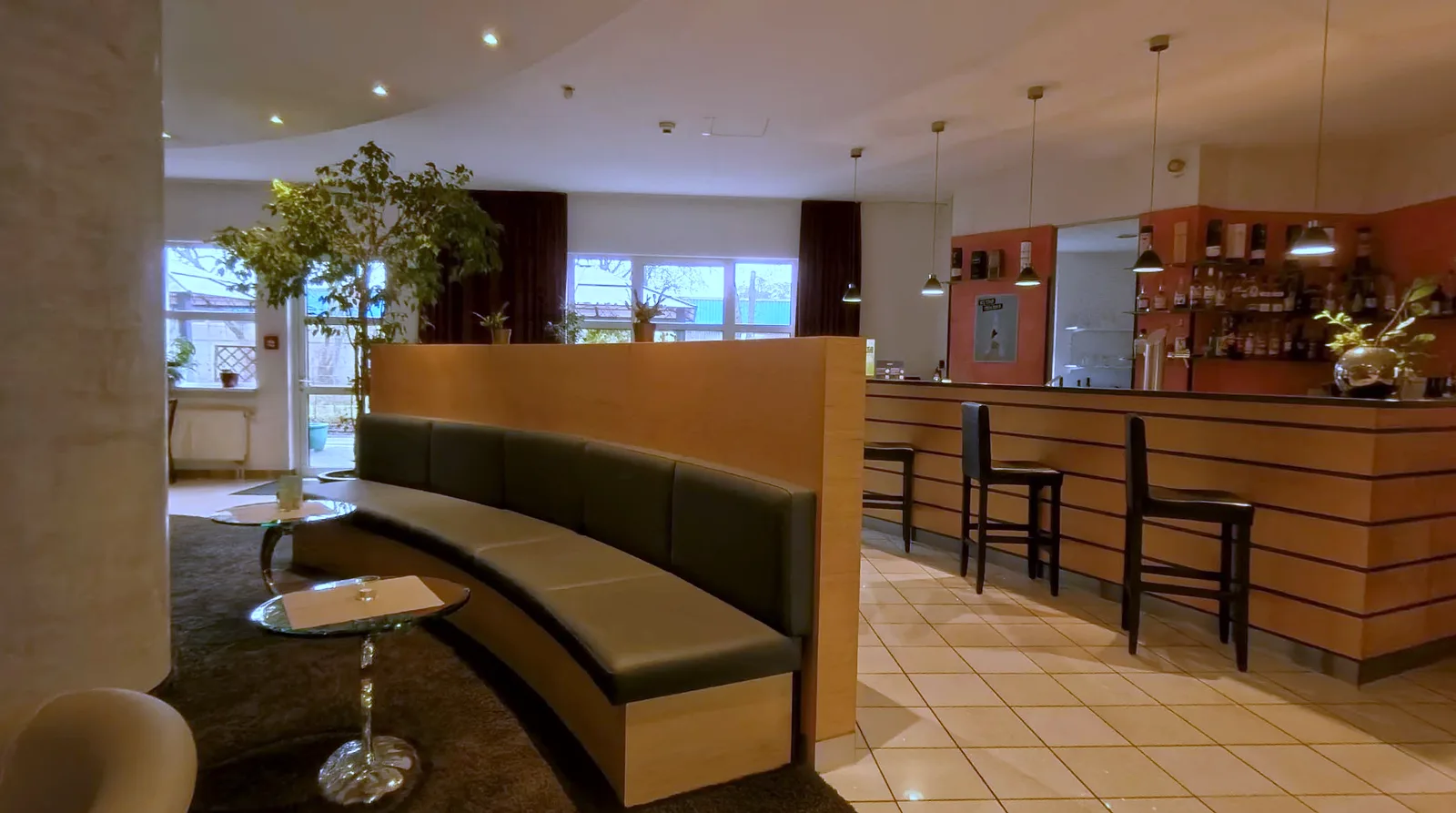 Lobby lounge at the EURO PARK HOTEL Hennef with a curved bench, small glass tables, a bar counter with stools and a row of windows