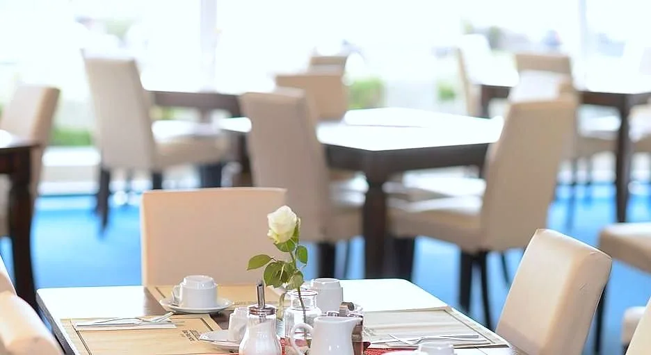 Eingedeckter Tisch für Gäste des Frühstücksbuffets mit Tassen, Milchkännchen, Zuckerstreuer und weißer Rose im Restaurant des EURO PARK HOTEL Hennef