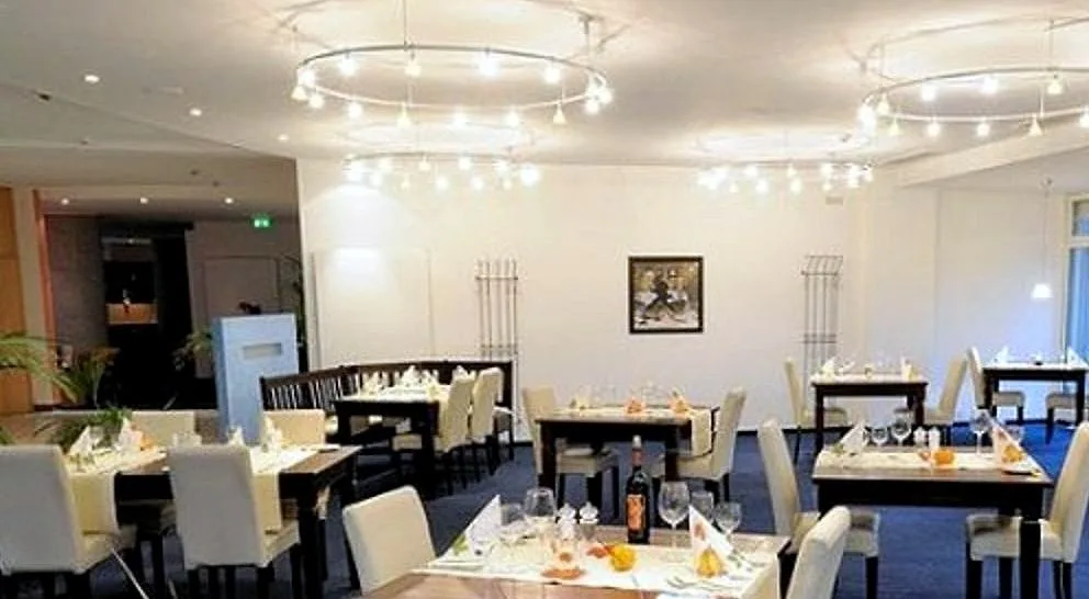 Restaurant im EURO PARK HOTEL Hennef mit leuchtenden Ringleuchtern, gedeckten Holztischen mit Gläsern und Flasche und cremefarbenen Stühlen