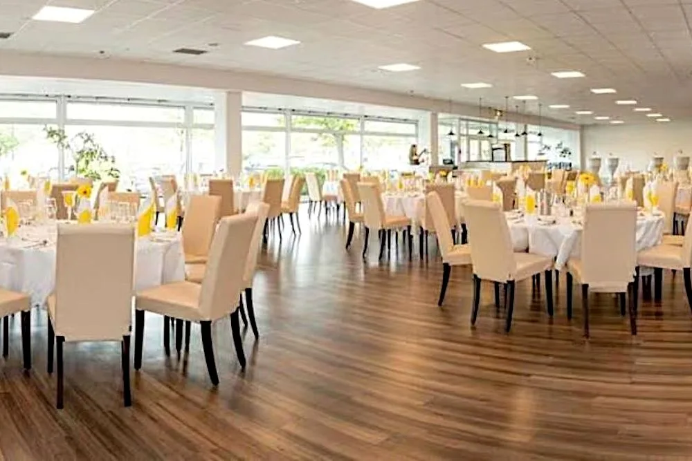Veranstaltungssaal im EURO PARK HOTEL Hennef mit vielen runden Tischen, hellen Polsterstühlen, gelben Servietten, Sonnenblumen und langer Fensterfront