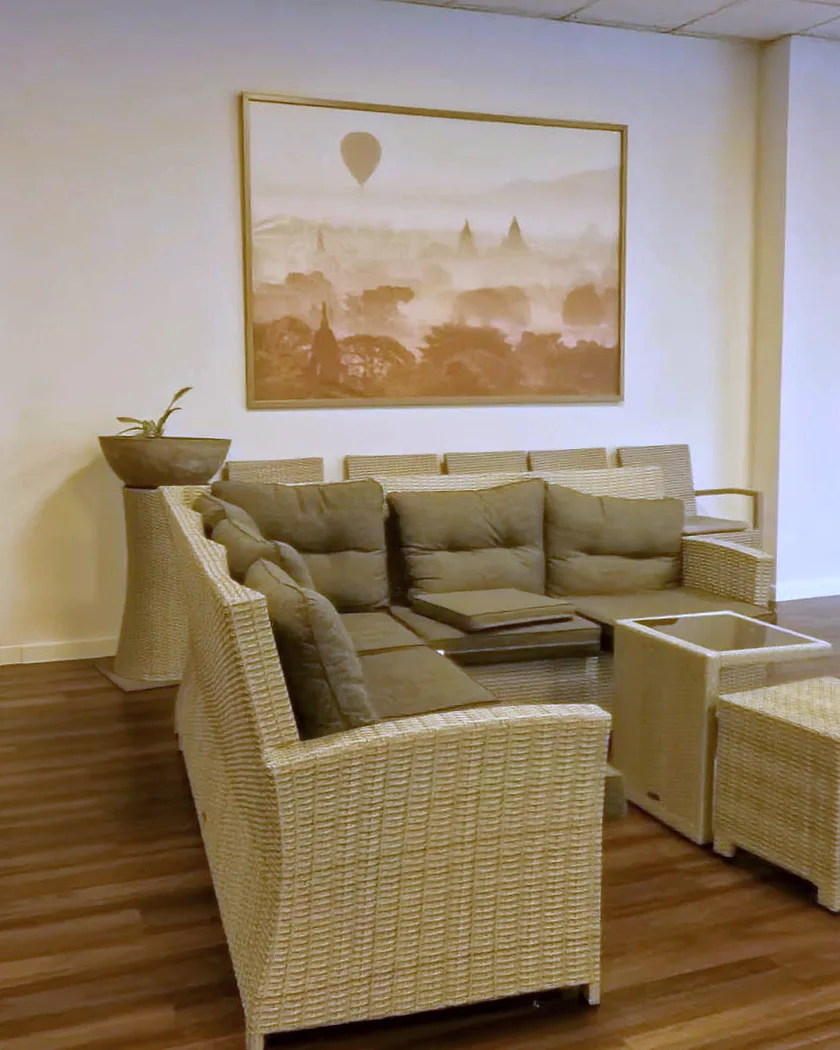 Sitzecke im Veranstaltungssaal des EURO PARK HOTEL Hennef: Rattansofa mit Kissen, ein Tisch mit Glasplatte, ein Hocker und ein Bild mit Heißluftballon