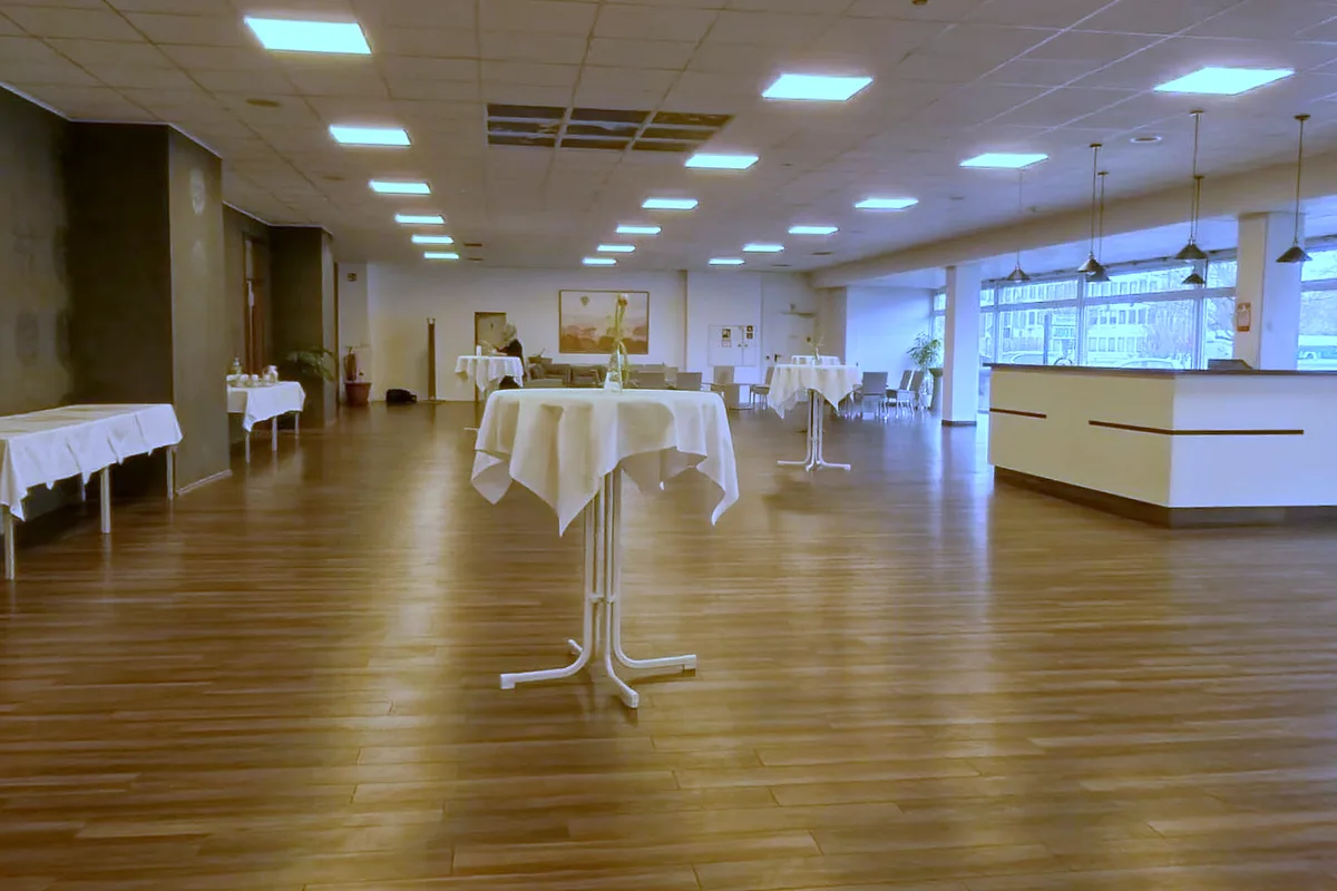 Großer Veranstaltungssaal im EURO PARK HOTEL Hennef mit Boden in Holzoptik, Stehtischen mit weißen Decken, heller Theke und langer Fensterfront