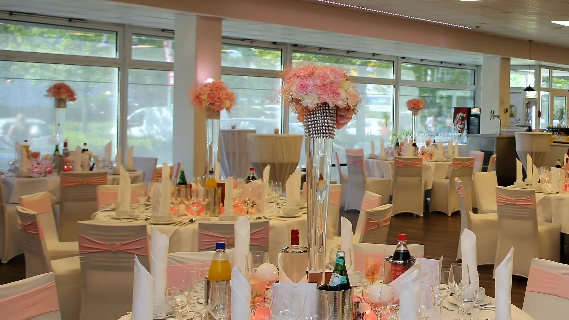 Veranstaltungssaal im EURO PARK HOTEL Hennef, festlich eingedeckt mit runden Tischen, rosa Stuhlschleifen und hohen Blumengestecken vor der Fensterfront