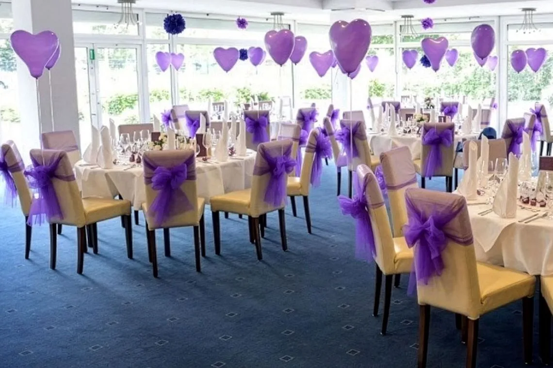 Festlich dekorierter Raum im EURO PARK HOTEL Hennef mit runden Tischen, Stühlen mit lila Schleifen und lila Herzballons vor der Fensterfront