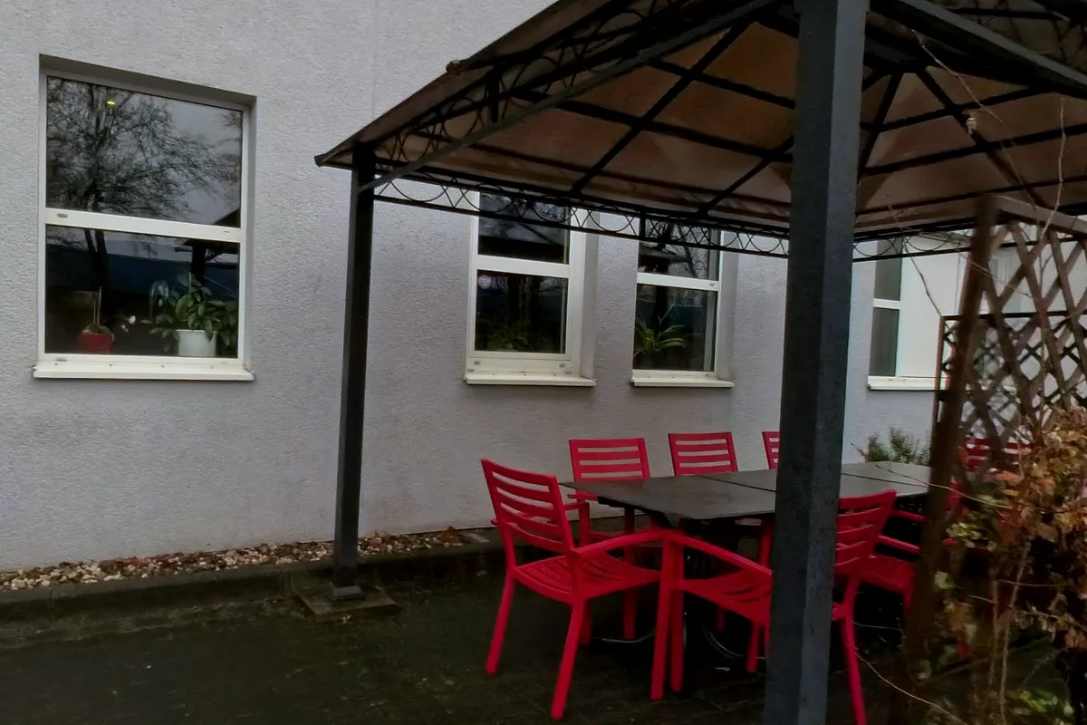 Pavillon auf der Terrasse des EURO PARK HOTEL Hennef mit roten Stühlen und dunklem Tisch, rechts ein Rankgitter, links die helle Hausfassade mit Fenstern