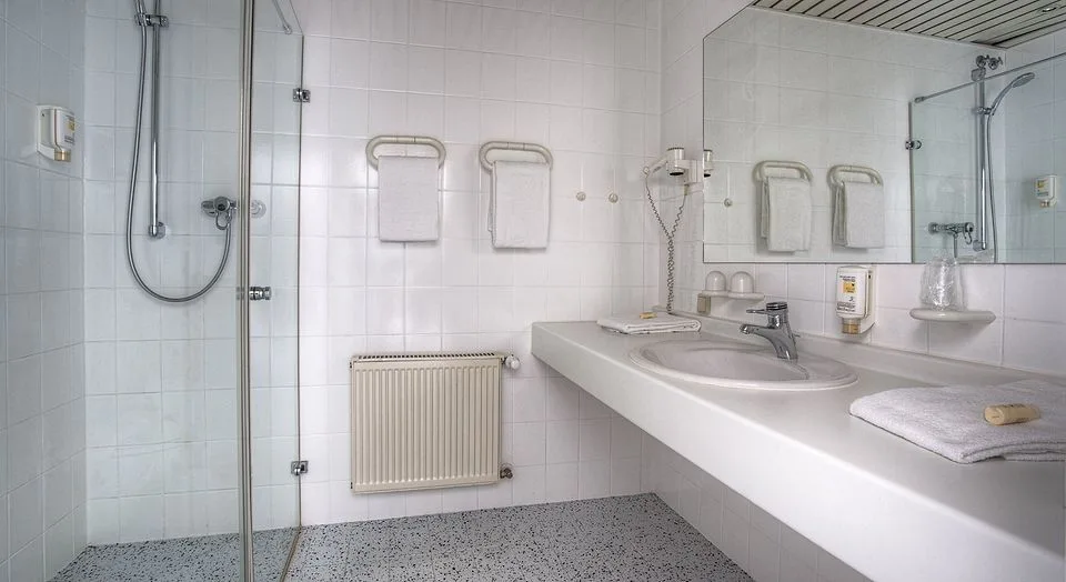 Gästebad im EURO PARK HOTEL Hennef mit verglaster Dusche, Handtuchhaltern, langem Waschtisch, großem Spiegel und Föhn an der Wand