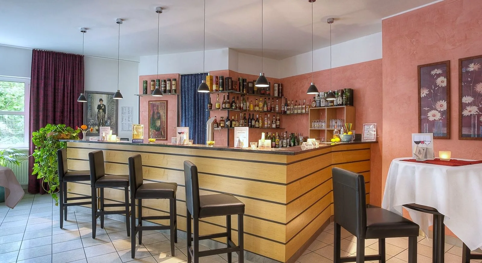 Hotelbar im EURO PARK HOTEL Hennef: Holztheke mit dunklen Barhockern, Flaschenregale an lachsfarbener Wand und Hängeleuchten