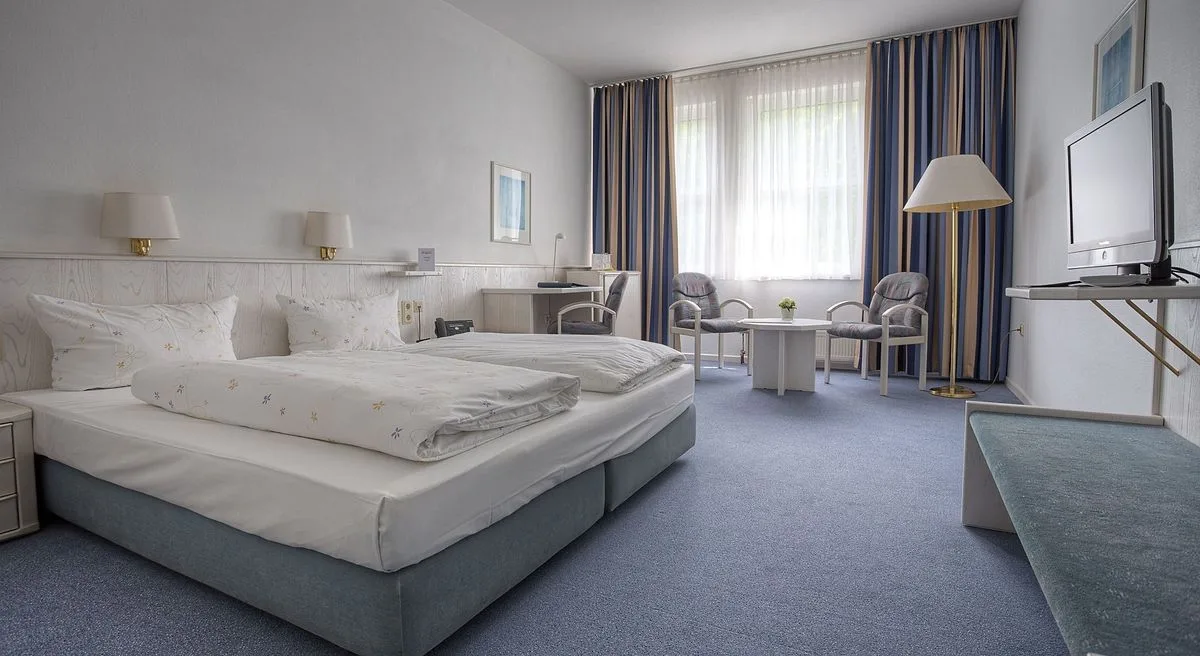 Standardzimmer im EURO PARK HOTEL Hennef mit zwei zusammengestellten Betten, blauem Teppich, Schreibtisch, Sitzecke am Fenster und Fernseher