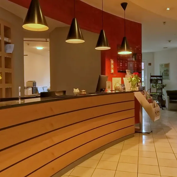 Reception at EURO PARK HOTEL Hennef with a curved wooden counter, black pendant lights, a red wall and a bunch of flowers on the desk