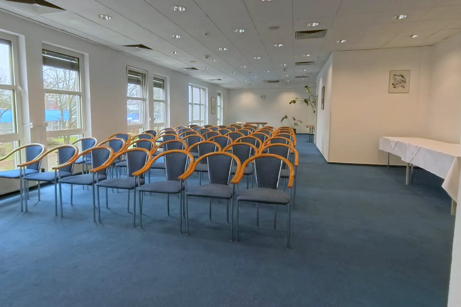 Seminar room at EURO PARK HOTEL Hennef with rows of blue upholstered chairs, blue carpet and tall windows looking out onto trees