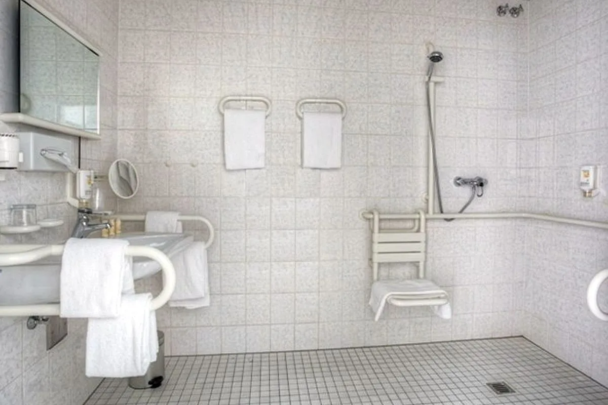 Accessible bathroom at EURO PARK HOTEL Hennef with an open shower, a fold-down shower seat, wall grab rails and a washbasin with support rails