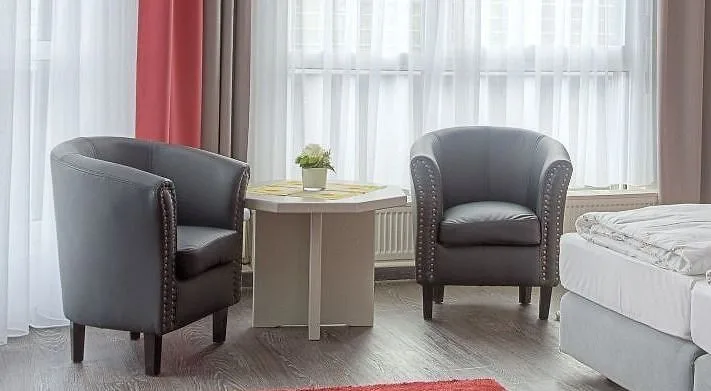 Seating corner in a comfort room at EURO PARK HOTEL Hennef with two grey armchairs, a small table with a potted flower and light curtains