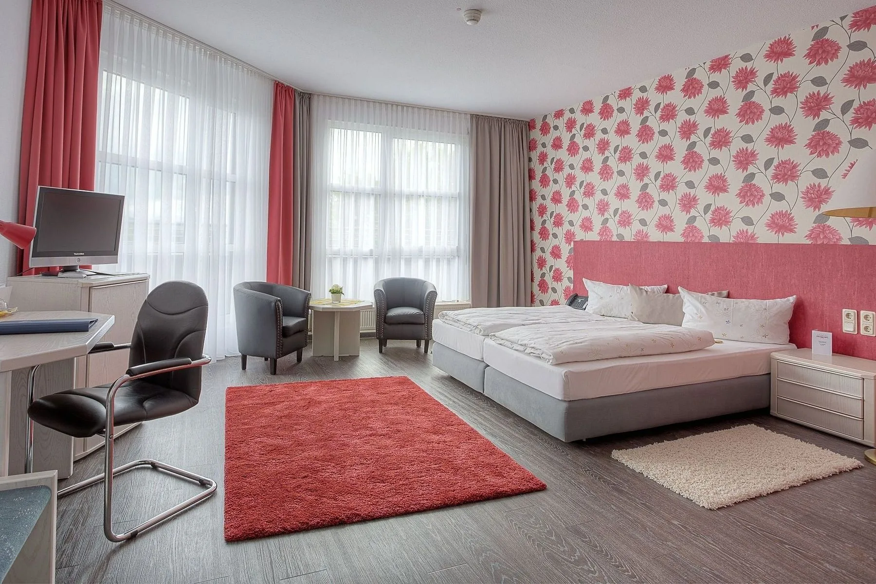Comfort room at EURO PARK HOTEL Hennef with a double bed against red floral wallpaper, a red rug, a desk and two armchairs by the window