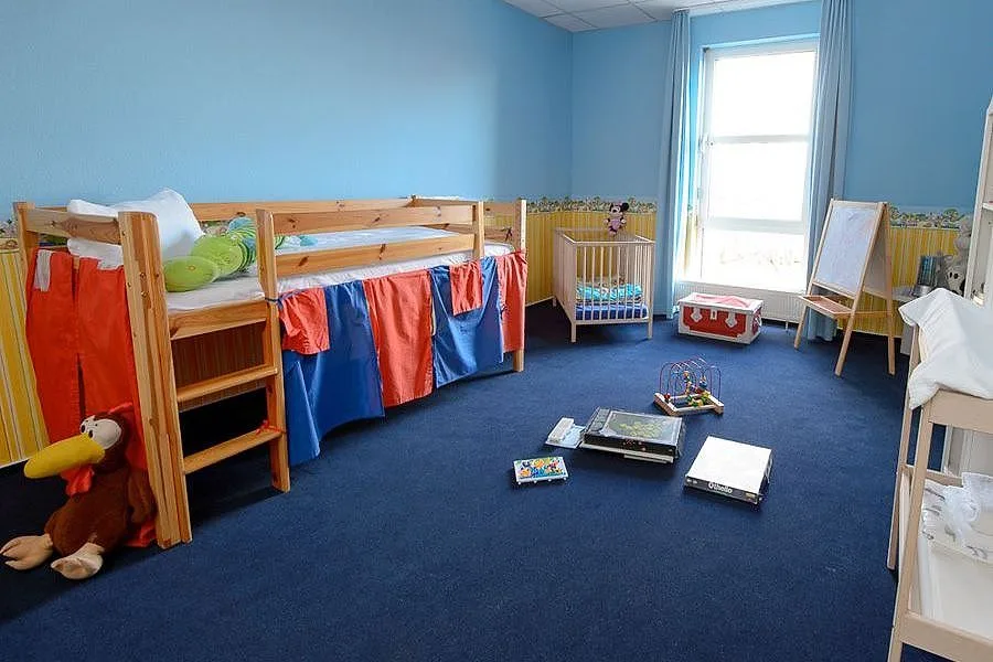 Kinderbereich im Familienzimmer des EURO PARK HOTEL Hennef mit Hochbett, Babybett, Maltafel, Wickelregal und Spielsachen auf blauem Teppich